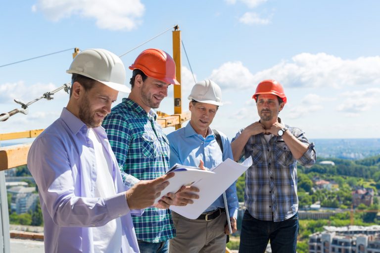 Group Of Builders In Hardhats Meeting On Construction Site Building Team Working With Plan Engineer